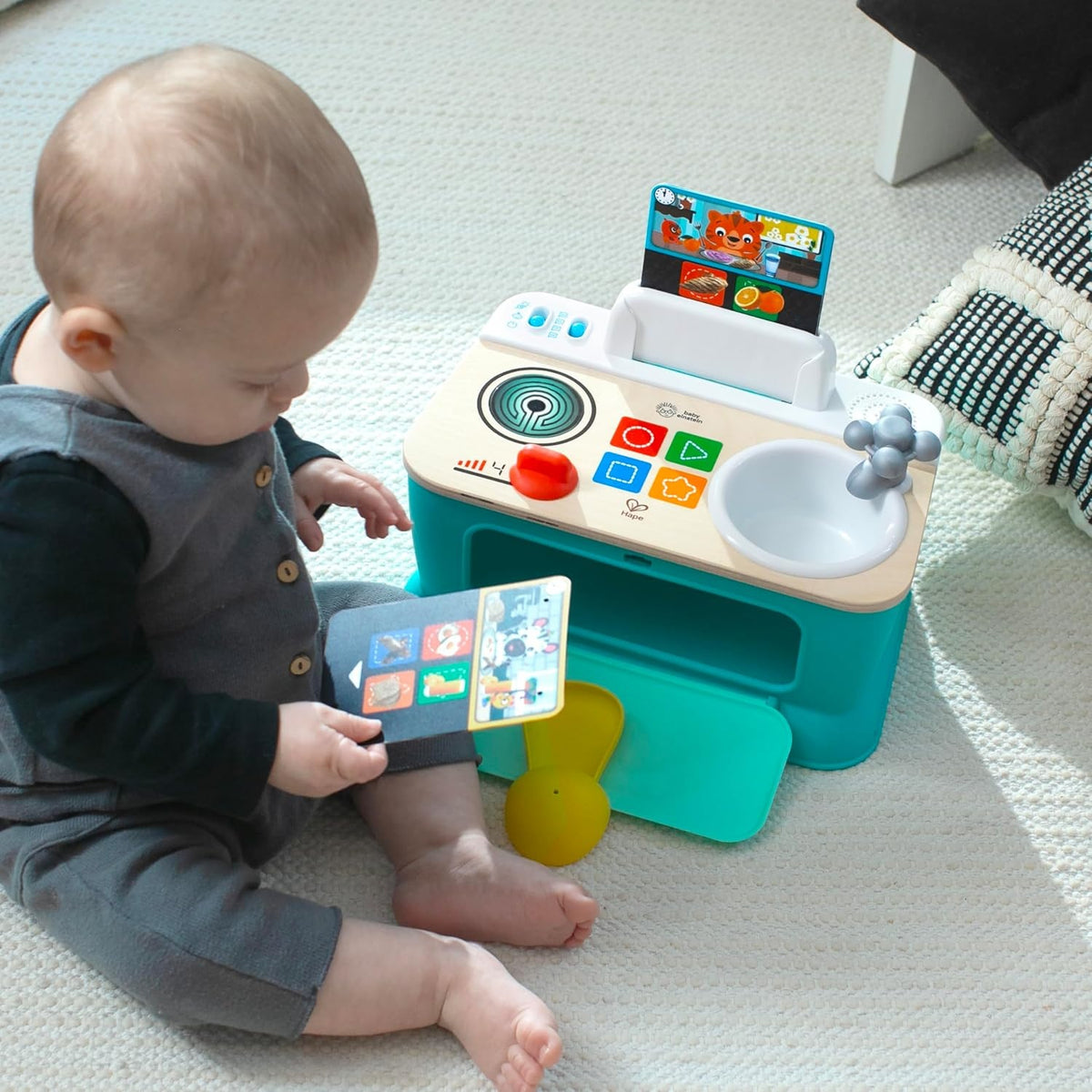 Dziecko siedzące obok kuchni Baby Einstein Hape i trzymające kartę obrazkową.