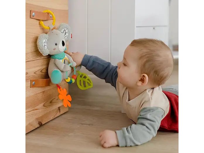 Dziecko sięga do zabawki FEHN DoBabyDoo Koala zawieszonej żółtym pierścieniem przy drewnianej konstrukcji.